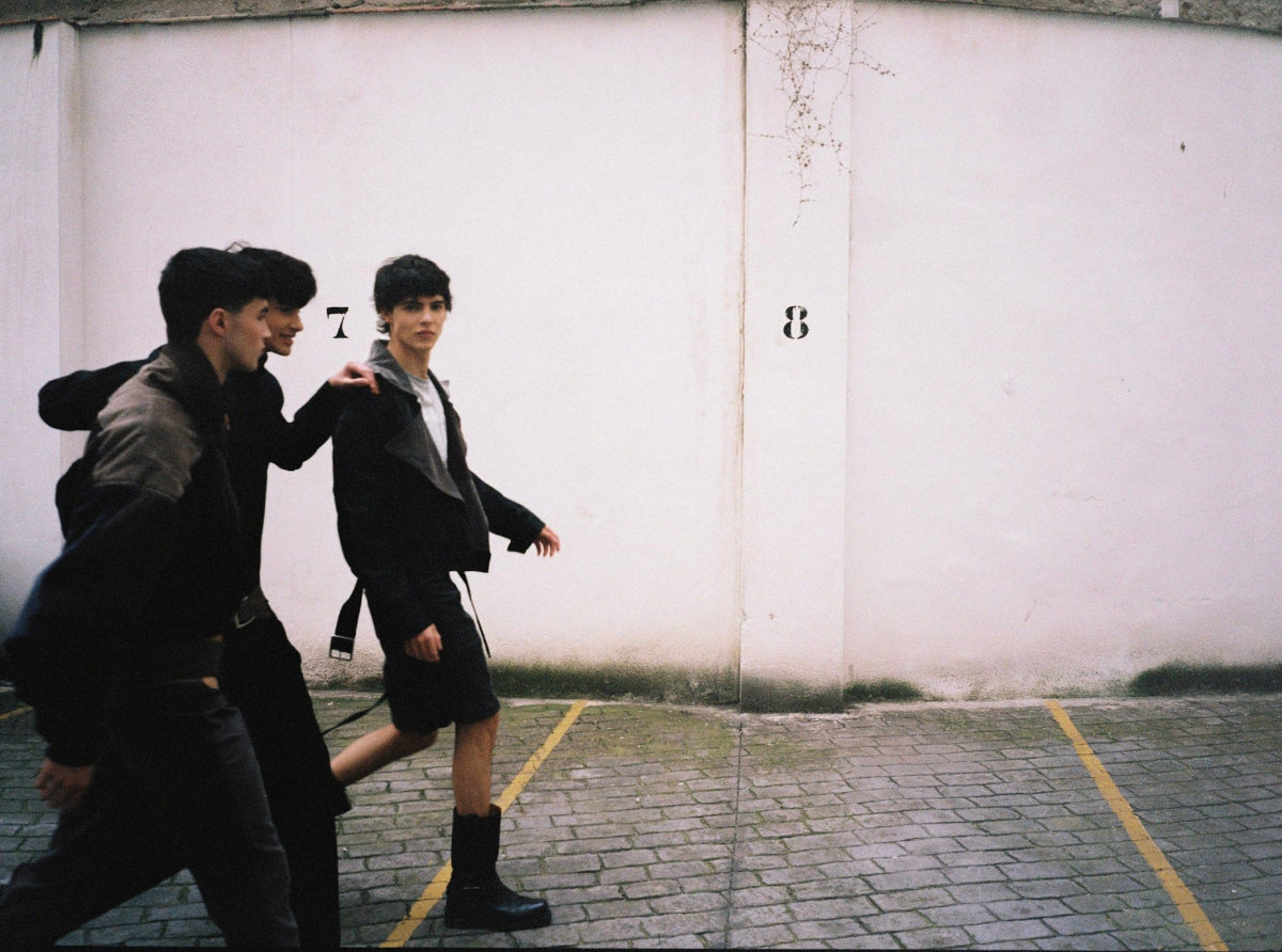 Three people wearing Juan VG clothes walking in a parking lot with a white wall in the background